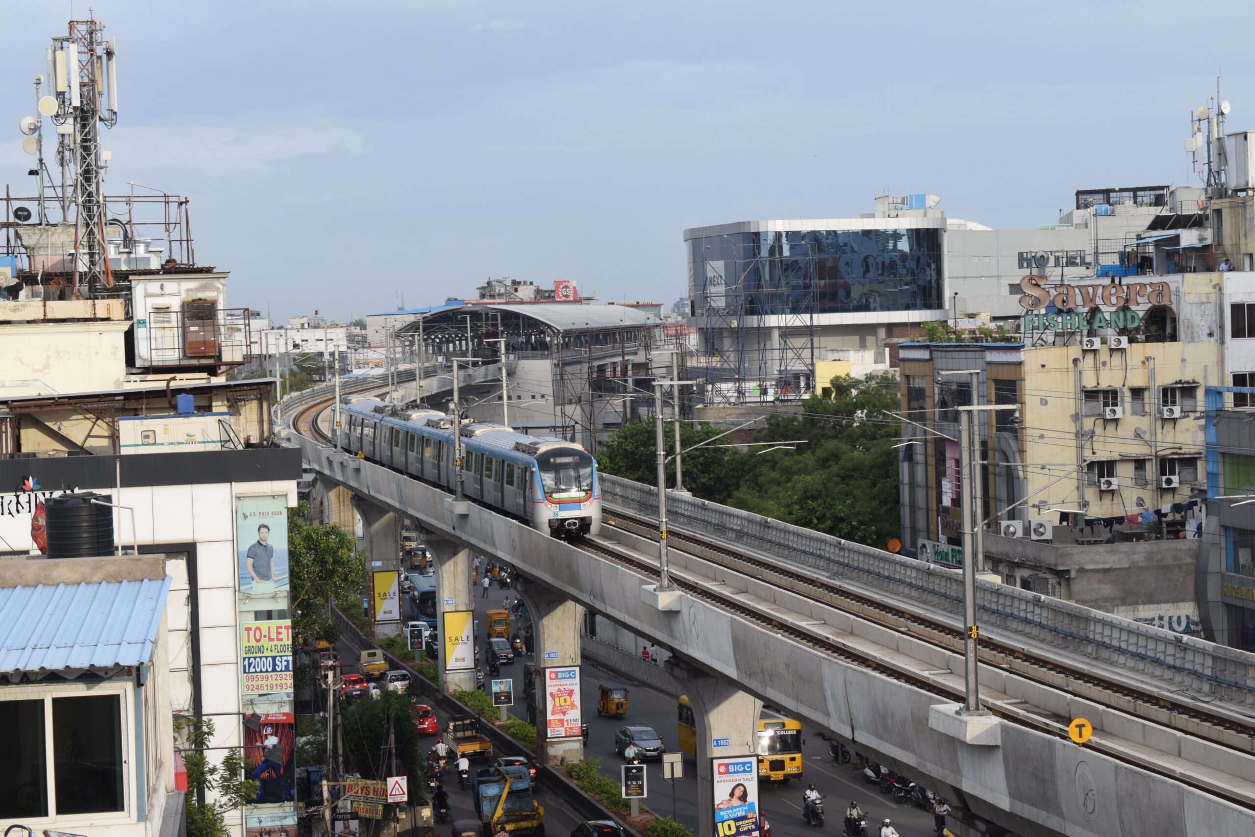 Hyderabad metro train navigating elevated tracks with city buildings and traffic below.