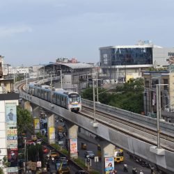 Hyderabad metro train navigating elevated tracks with city buildings and traffic below.