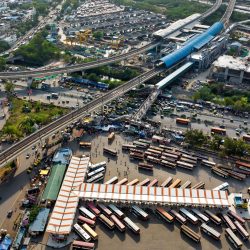 Aerial view of urban transport hub with multiple buses and highway bridges in daylight.