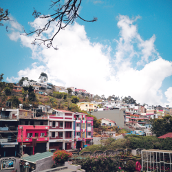 Vibrant hillside town with colorful buildings against a bright blue sky and fluffy clouds.